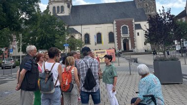 Ältere Menschen auf einem Platz, im Hintergrund eine Kirche.